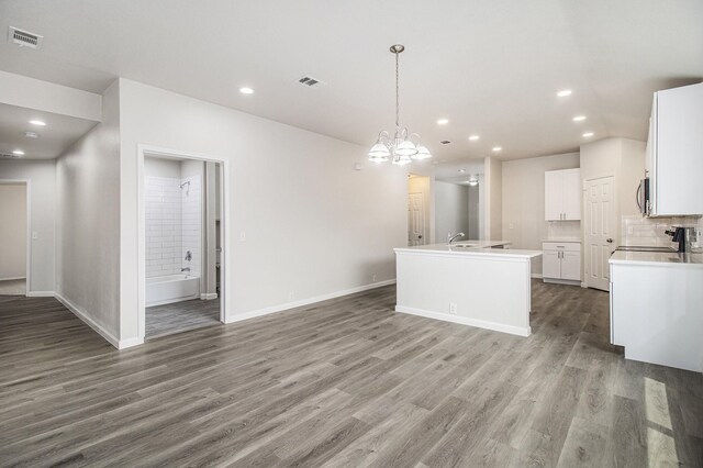 kitchen featuring white cabinets, pendant lighting, decorative backsplash, an island with sink, and wood-type flooring