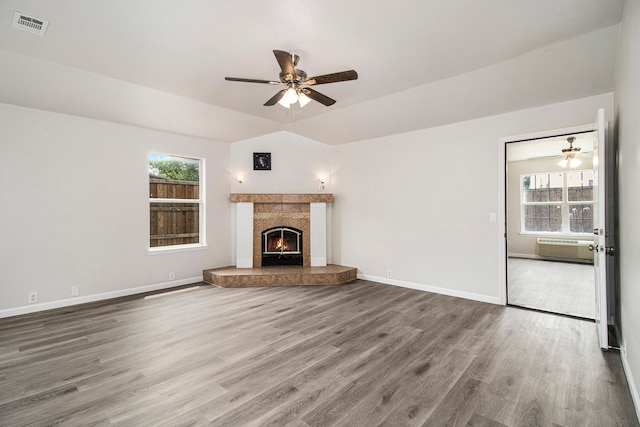 unfurnished living room with an AC wall unit, a tiled fireplace, ceiling fan, and hardwood / wood-style floors