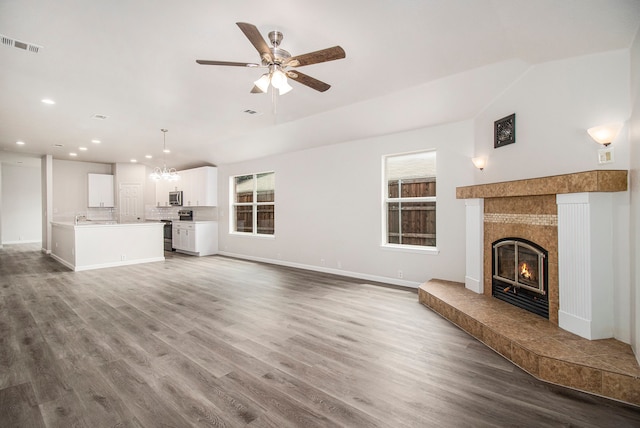 unfurnished living room featuring a tiled fireplace, ceiling fan with notable chandelier, and light wood-type flooring