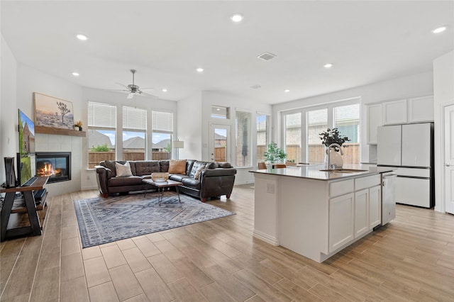 kitchen featuring white cabinets, light wood-type flooring, refrigerator, and a center island with sink