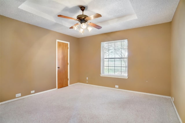 carpeted spare room with a textured ceiling, ceiling fan, and a tray ceiling