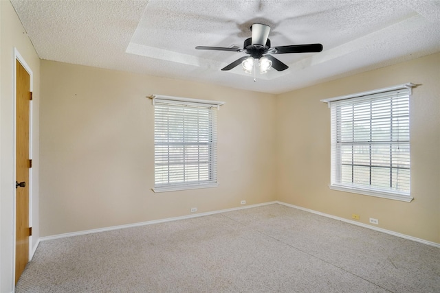 carpeted spare room with a textured ceiling, ceiling fan, and a raised ceiling