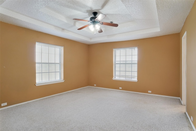 spare room featuring carpet floors, ceiling fan, plenty of natural light, and a tray ceiling