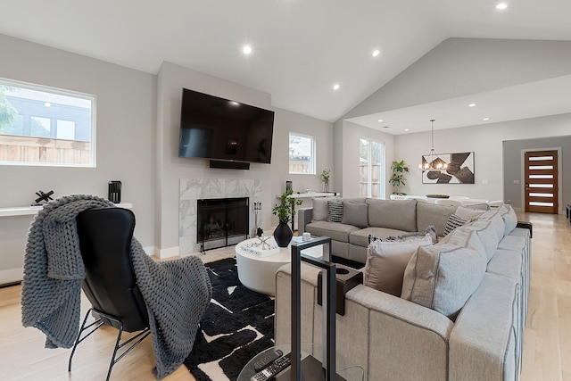 living room featuring a high end fireplace, a chandelier, high vaulted ceiling, and light wood-type flooring