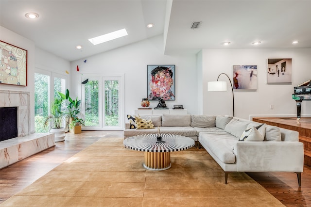 living room with a fireplace, light hardwood / wood-style flooring, and vaulted ceiling with skylight