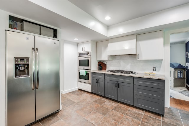 kitchen with stainless steel appliances, custom range hood, light hardwood / wood-style flooring, backsplash, and gray cabinetry