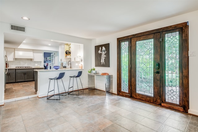 kitchen with white cabinetry, tasteful backsplash, kitchen peninsula, a kitchen bar, and light tile patterned floors