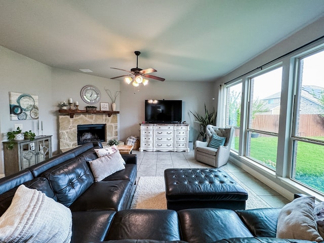 living room featuring a stone fireplace, light tile patterned floors, and ceiling fan