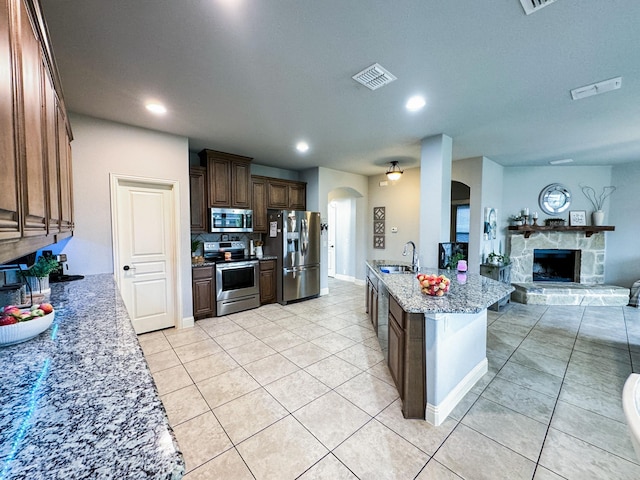 kitchen featuring a stone fireplace, sink, light tile patterned floors, appliances with stainless steel finishes, and light stone countertops