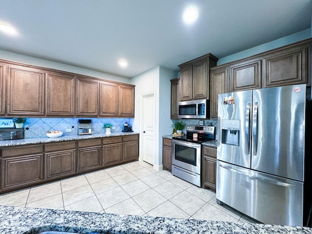 kitchen featuring light tile patterned floors, decorative backsplash, light stone countertops, and appliances with stainless steel finishes