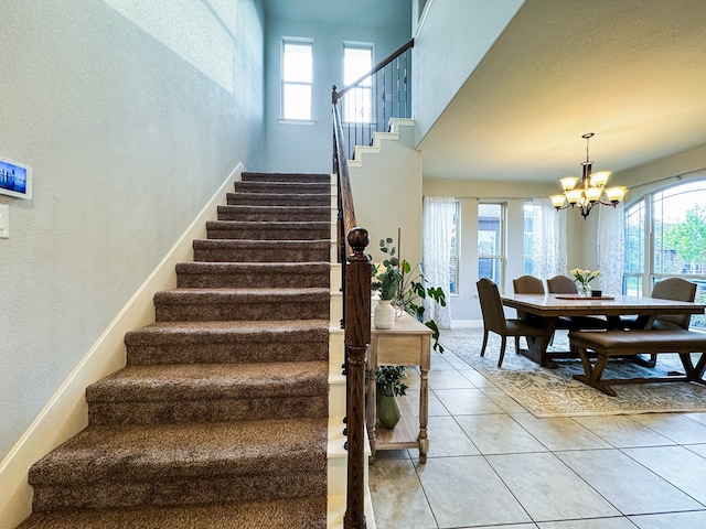 stairway featuring an inviting chandelier, a towering ceiling, light tile patterned floors, and plenty of natural light