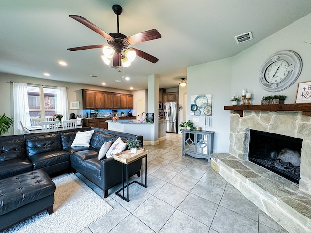 living room with a stone fireplace, light tile patterned floors, and ceiling fan