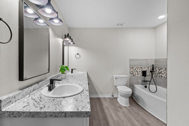 bathroom featuring toilet, a tub to relax in, hardwood / wood-style flooring, and dual bowl vanity