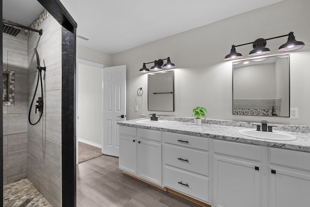 bathroom featuring tiled shower, hardwood / wood-style flooring, and dual bowl vanity