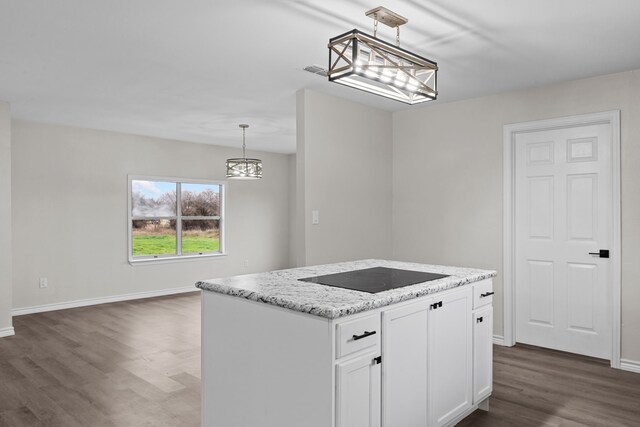 kitchen with stovetop, decorative light fixtures, light stone countertops, a center island, and wood-type flooring