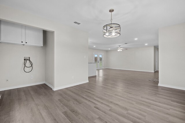 unfurnished living room with ceiling fan with notable chandelier and light hardwood / wood-style flooring