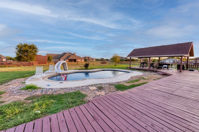 view of swimming pool with a water slide, a yard, and a wooden deck