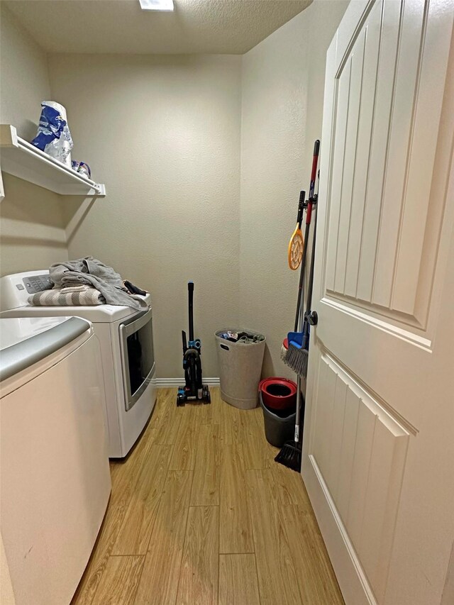 clothes washing area with light hardwood / wood-style floors, washer and clothes dryer, and a textured ceiling