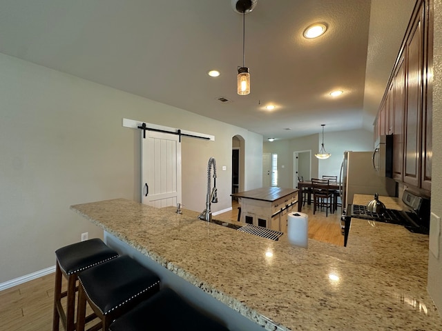 kitchen with range, light stone counters, hanging light fixtures, a barn door, and light hardwood / wood-style floors