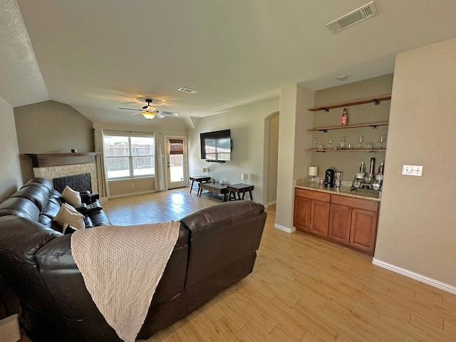 living room with a fireplace, light hardwood / wood-style floors, lofted ceiling, and ceiling fan