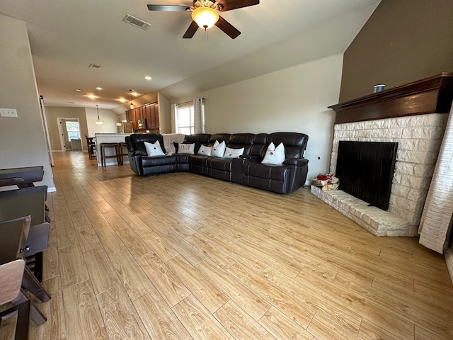 living room with a fireplace, light wood-type flooring, ceiling fan, and vaulted ceiling