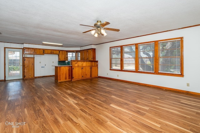 unfurnished living room featuring dark wood-type flooring, ceiling fan, crown molding, and a textured ceiling