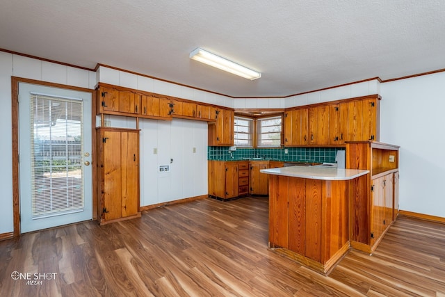 kitchen with crown molding, wood-type flooring, kitchen peninsula, and a textured ceiling