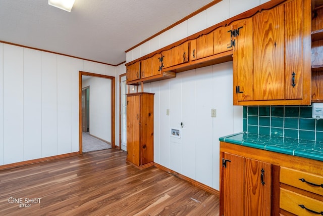 kitchen with hardwood / wood-style flooring, ornamental molding, a textured ceiling, decorative backsplash, and tile countertops