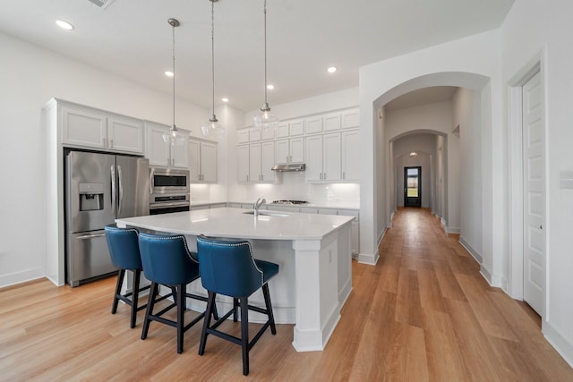 kitchen with arched walkways, under cabinet range hood, stainless steel appliances, a sink, and light countertops