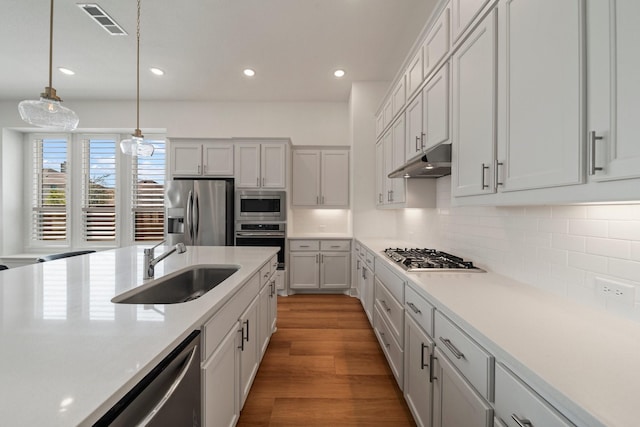 kitchen featuring a sink, under cabinet range hood, stainless steel appliances, light wood-style floors, and decorative backsplash