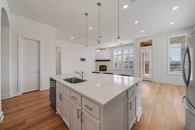 kitchen with a stone fireplace, an island with sink, sink, hanging light fixtures, and stainless steel appliances