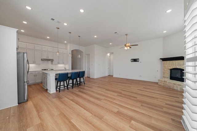 kitchen featuring pendant lighting, stainless steel refrigerator, a kitchen breakfast bar, ceiling fan, and a center island with sink