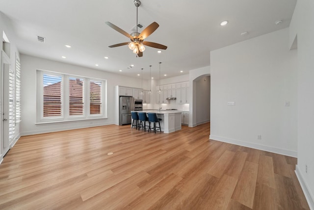 unfurnished living room featuring a ceiling fan, arched walkways, light wood-style flooring, and recessed lighting