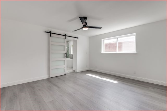 unfurnished bedroom featuring light hardwood / wood-style floors, a barn door, ensuite bath, and ceiling fan