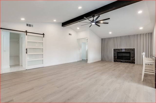 unfurnished living room featuring ceiling fan, vaulted ceiling with beams, a barn door, light hardwood / wood-style floors, and a high end fireplace