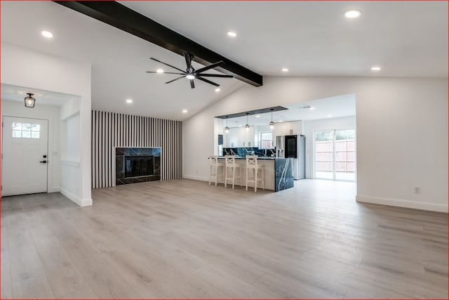 unfurnished living room with light hardwood / wood-style floors, beam ceiling, ceiling fan, and a tiled fireplace