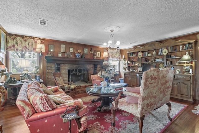 living room with dark wood-type flooring, a textured ceiling, a brick fireplace, and a notable chandelier