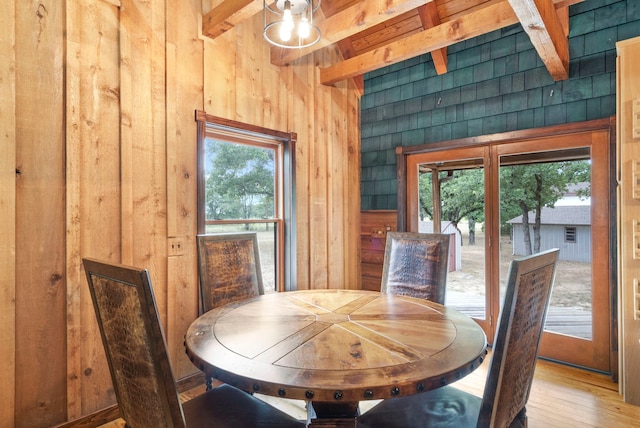 dining space featuring beamed ceiling, wood walls, a wealth of natural light, and light wood-type flooring