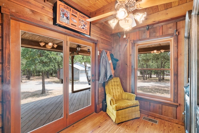 interior space with a healthy amount of sunlight, wood walls, light hardwood / wood-style floors, and beam ceiling