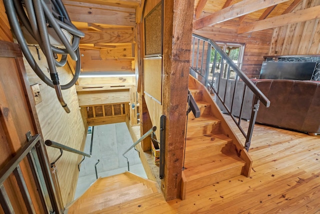 staircase with beamed ceiling, light hardwood / wood-style floors, and wood walls