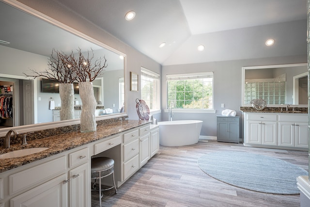 bathroom featuring vanity, hardwood / wood-style flooring, vaulted ceiling, and a tub