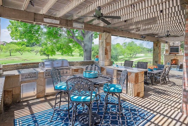 view of patio / terrace featuring area for grilling, ceiling fan, an outdoor stone fireplace, and a grill