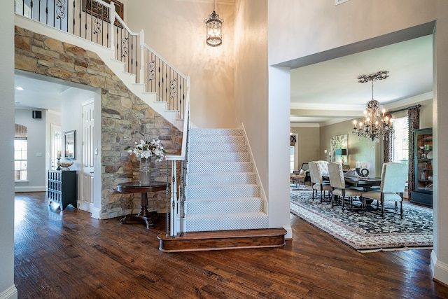 stairway featuring hardwood / wood-style floors, a towering ceiling, crown molding, and a chandelier