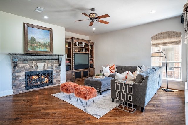 living room featuring a stone fireplace, ceiling fan, and dark wood-type flooring