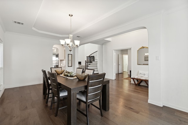 dining space featuring dark wood-type flooring, a raised ceiling, ornamental molding, and an inviting chandelier