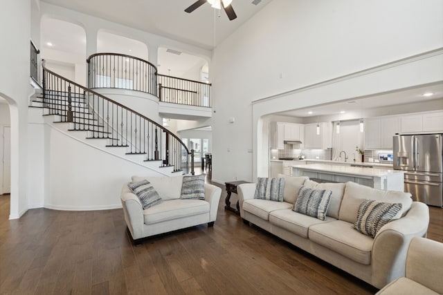 living room with dark wood-type flooring, a towering ceiling, and ceiling fan