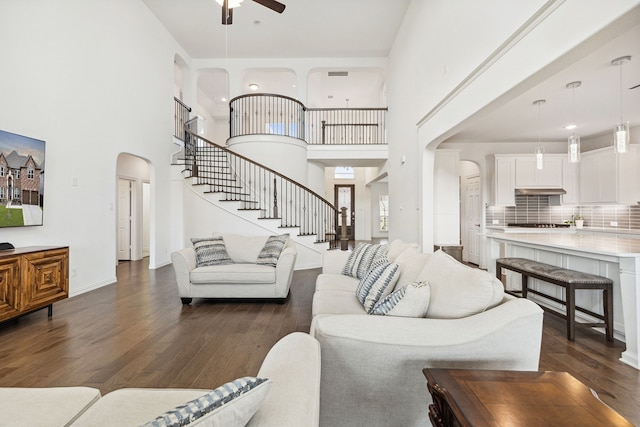 living room with dark wood-type flooring, ceiling fan, and a high ceiling