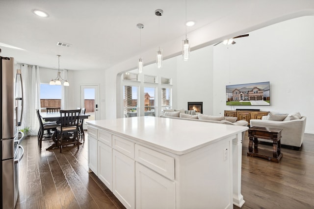 kitchen with dark wood-type flooring, hanging light fixtures, stainless steel fridge, a center island, and white cabinets