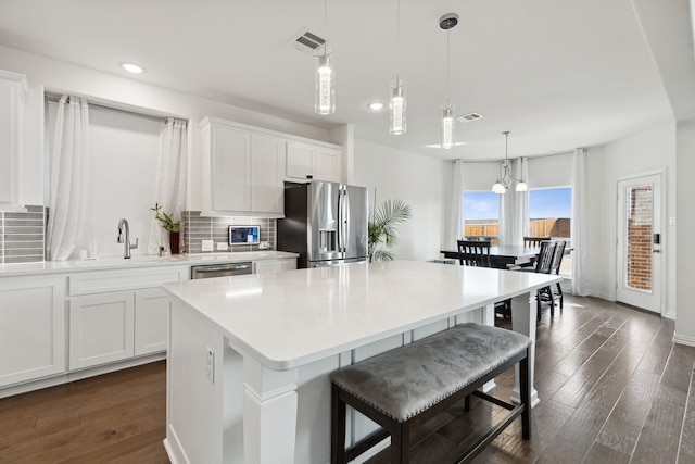 kitchen with hanging light fixtures, appliances with stainless steel finishes, white cabinetry, dark hardwood / wood-style floors, and a center island