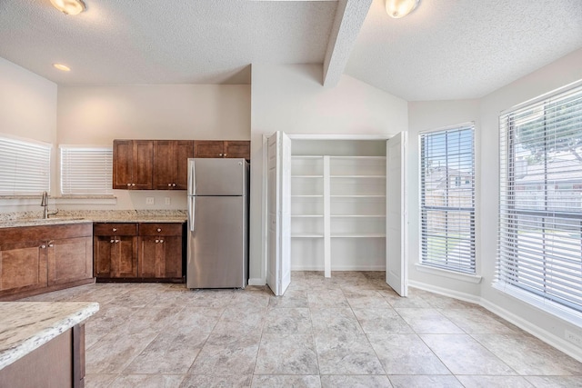 kitchen with stainless steel fridge, lofted ceiling with beams, a textured ceiling, and sink